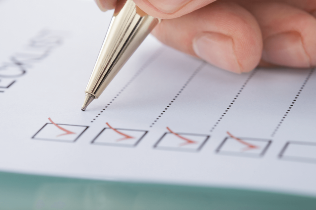 A checklist and hand holding a gold pen.