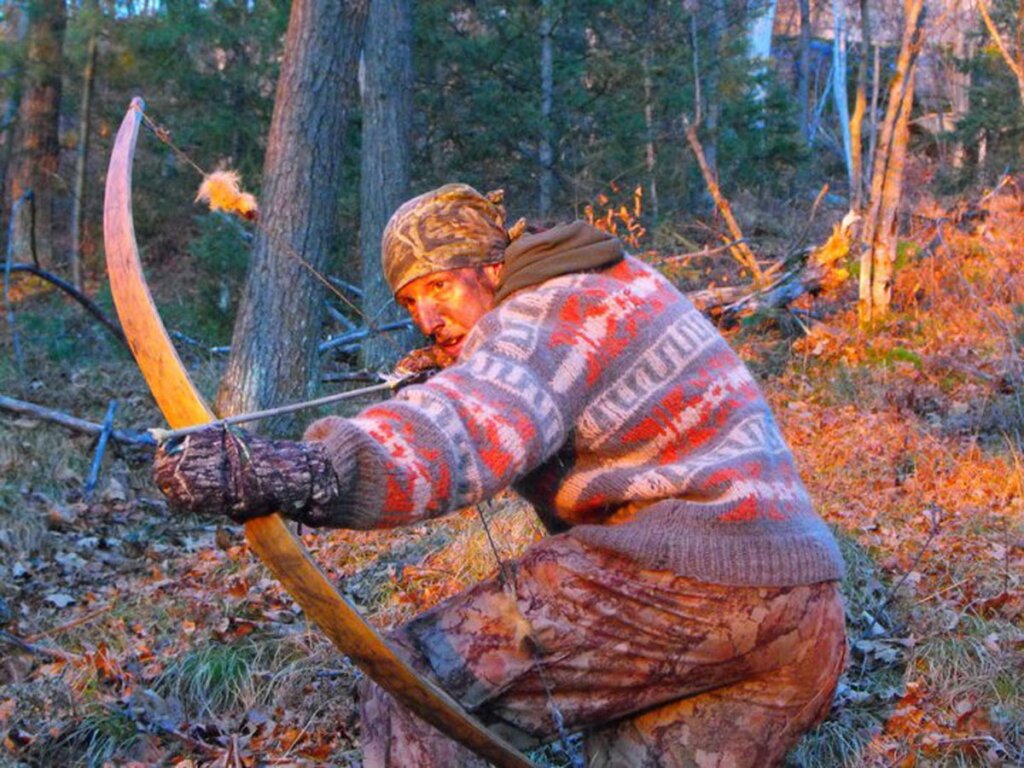 A man in the forest bow hunting.