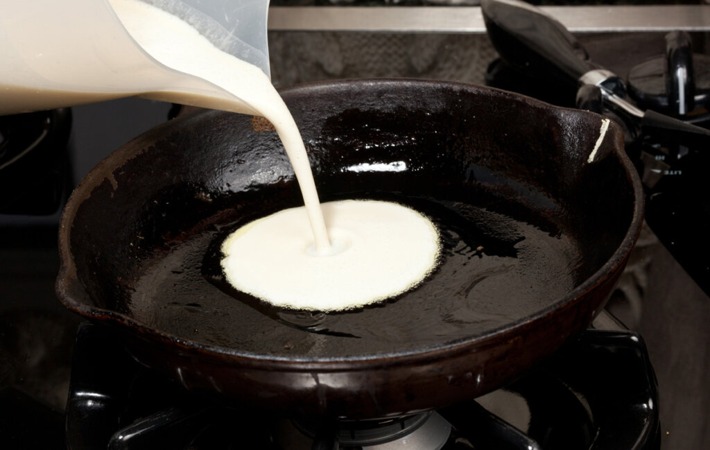 Pancake batter being poured into a hot cast iron skillet.