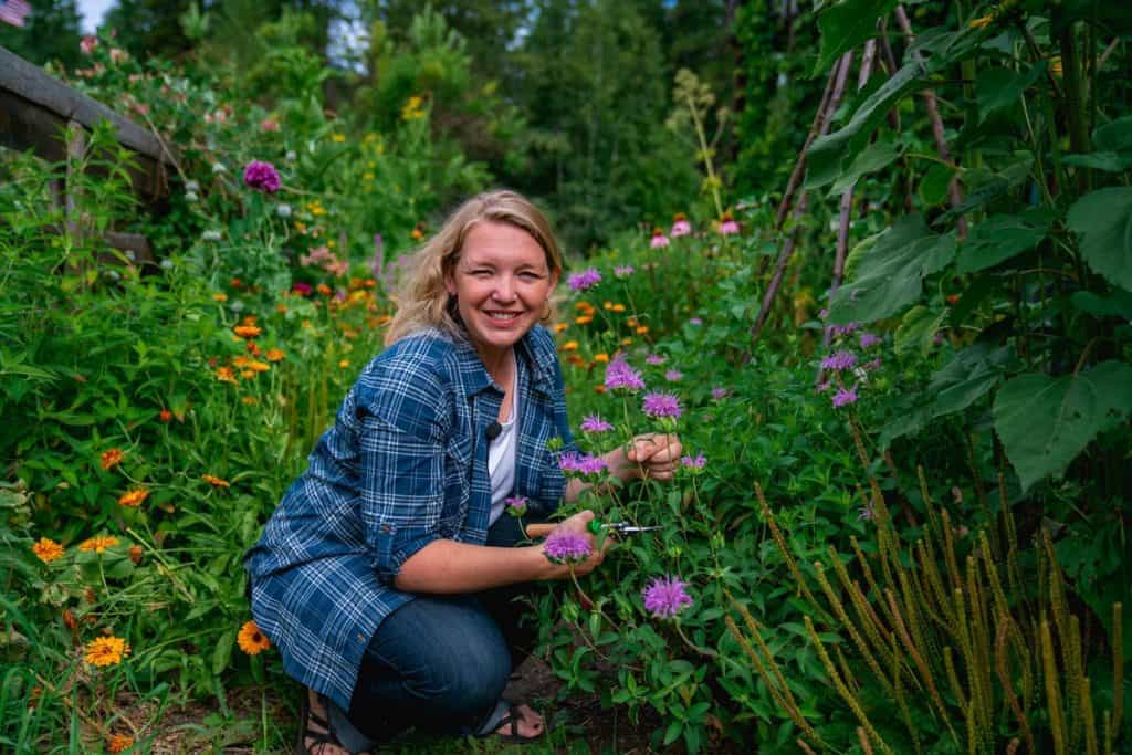 A woman cutting herbs and flowers from a cottage garden.