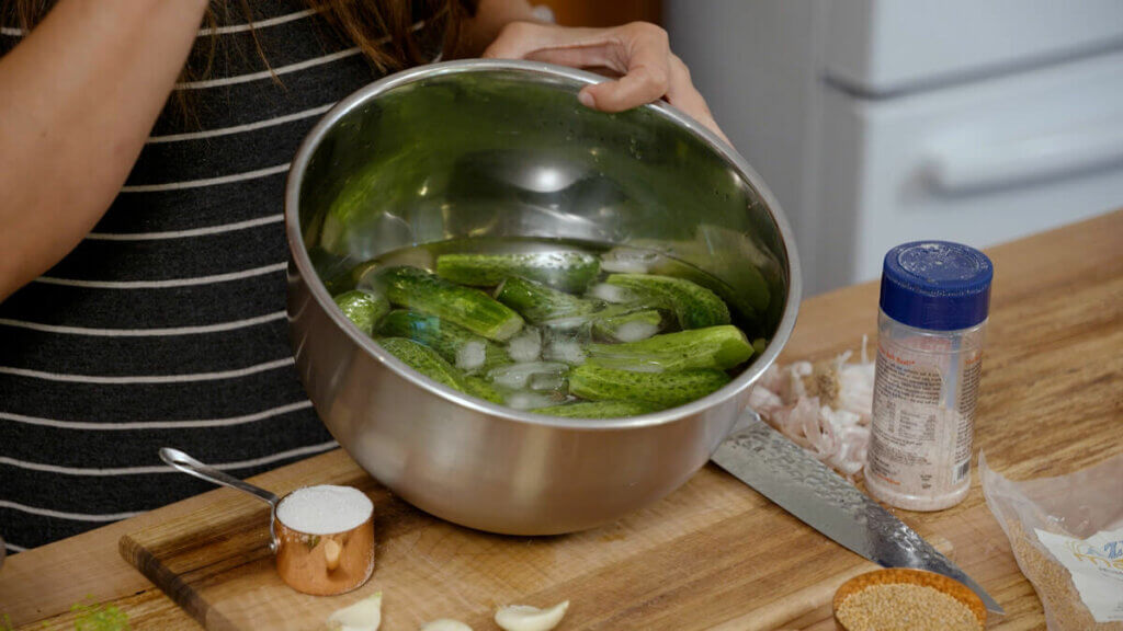 A stainless steel bowl filled with ice water and pickling cucumbers.