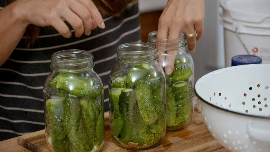A woman placing cucumbers in jars to make homemade pickles.