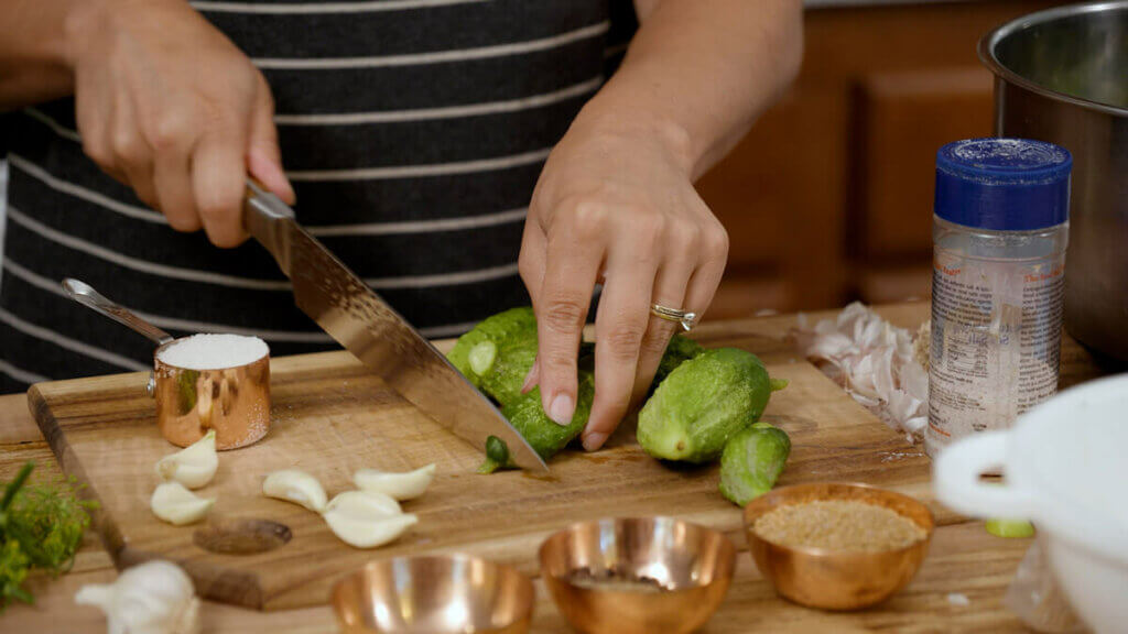 A woman cutting the ends off of pickling cucumbers.