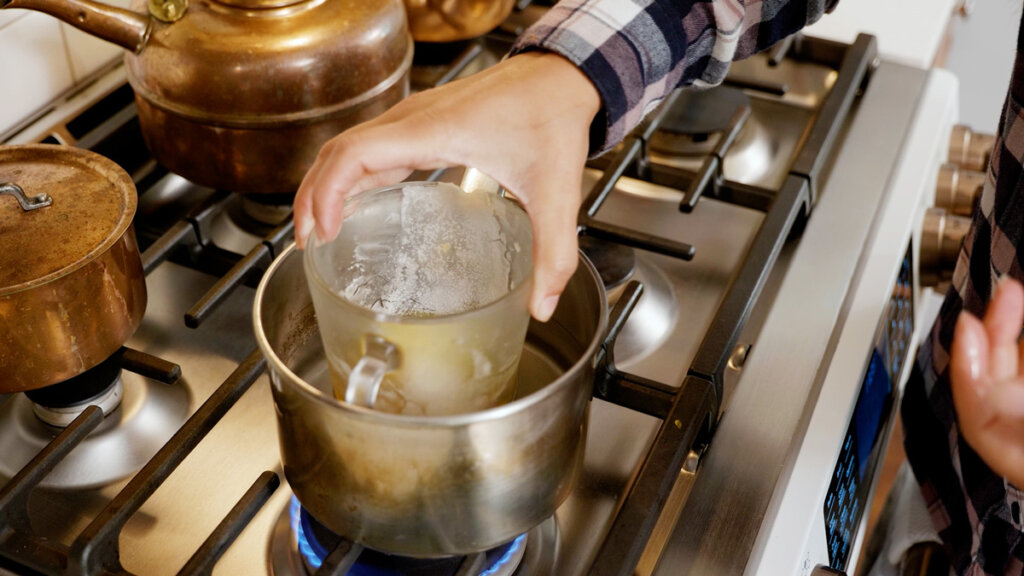 A Pyrex measuring cup in a double boiler on the stove.