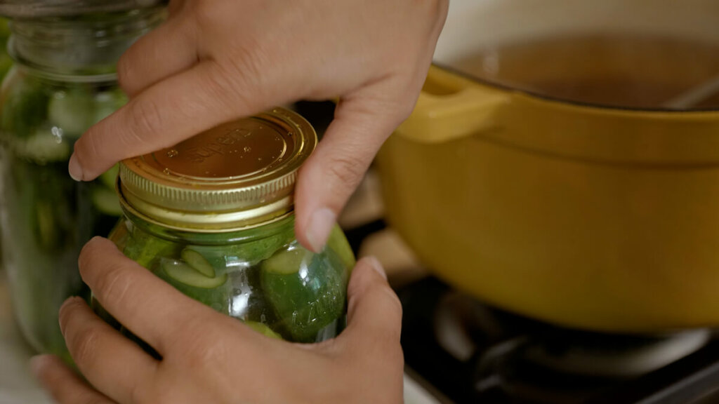A woman tightening a canning lid onto a jar.