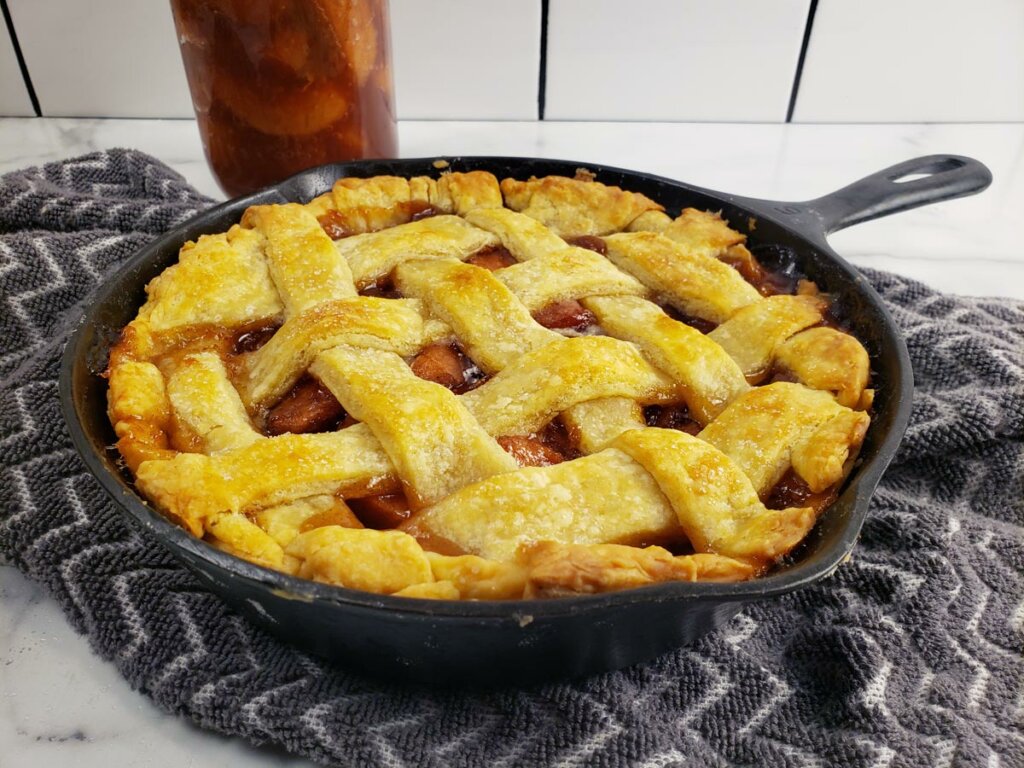 Apple pie with a lattice crust in a cast iron skillet with canned apple pie filling in the background.