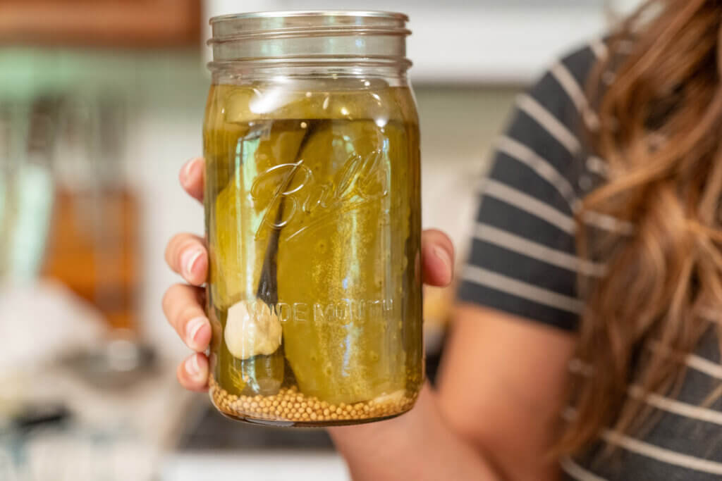 A woman holding a jar of garlic dill pickles.