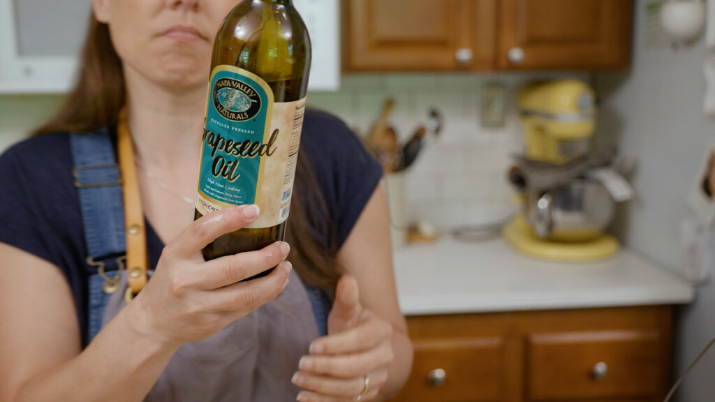 A woman holding up a bottle of grapeseed oil.