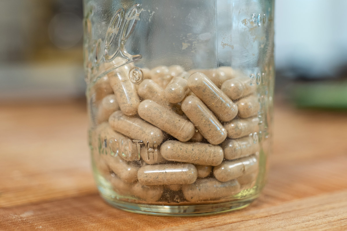 A jar of herbal capsules on a wooden counter.