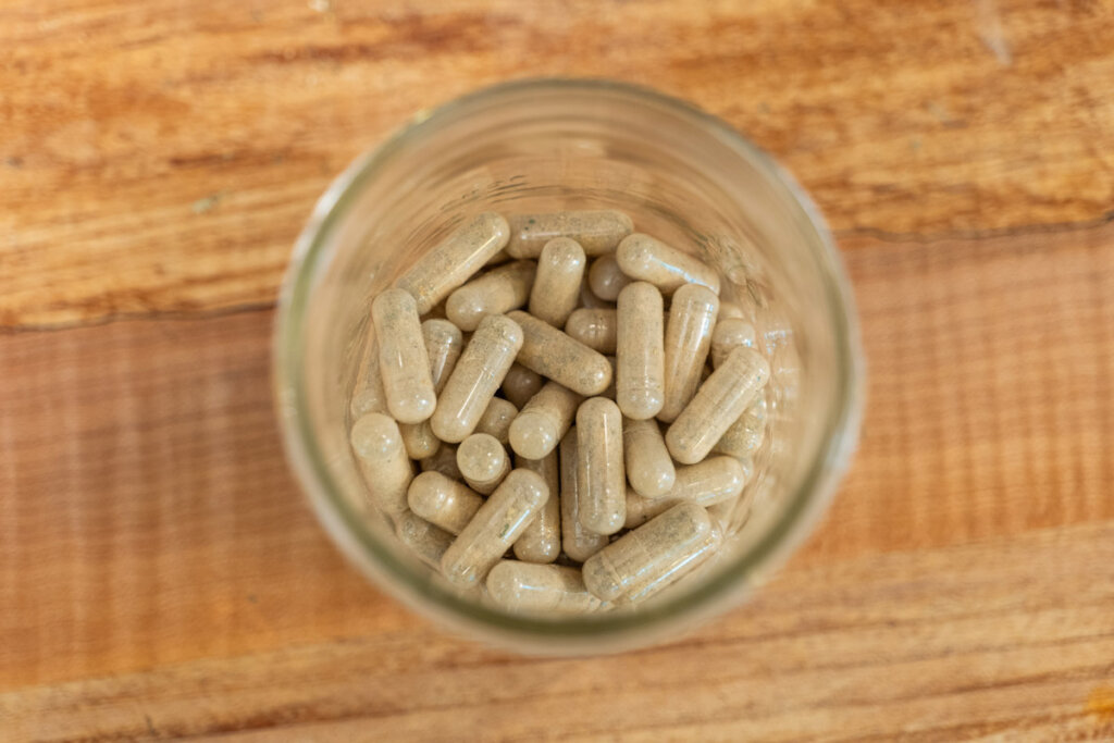 An overhead shot of a jar of herbal capsules on a wooden counter.
