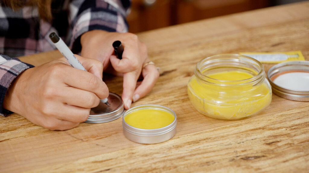 A woman labeling a tin of homemade healing salve.