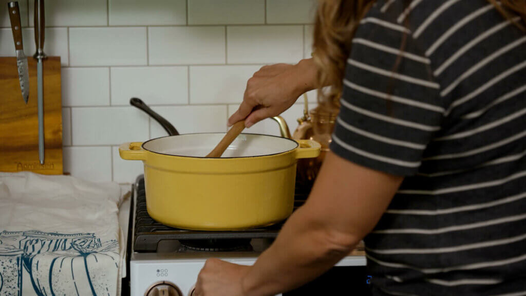 A woman stirring pickle brine in a large yellow pot on the stove.