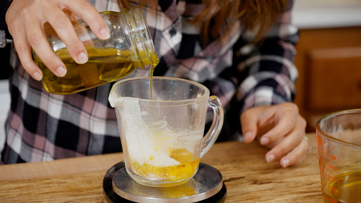 Calendula oil being poured into a Pyrex glass measuring cup.