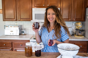 A woman holding a jar of fruit vinegar in the kitchen.