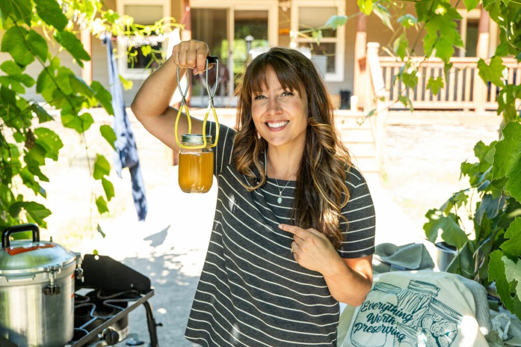 A woman outside holding up a jar of canned broth.