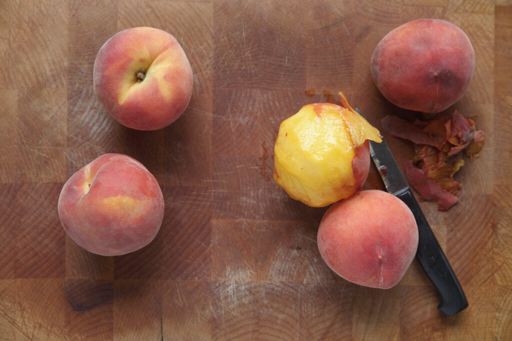 Peaches on a cutting board with a knife for peeling.