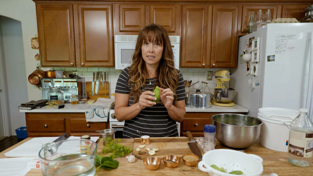 A woman with pickle ingredients on the counter in front of her.