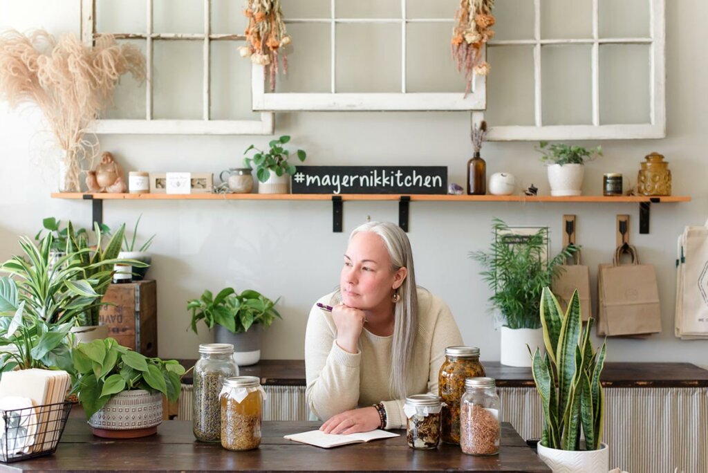 A woman in a kitchen with medicinal herbs around her.