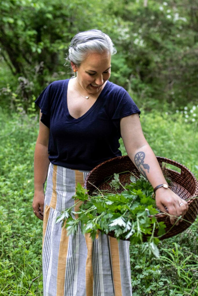 A woman in an herb garden with a basket of harvested herbs.