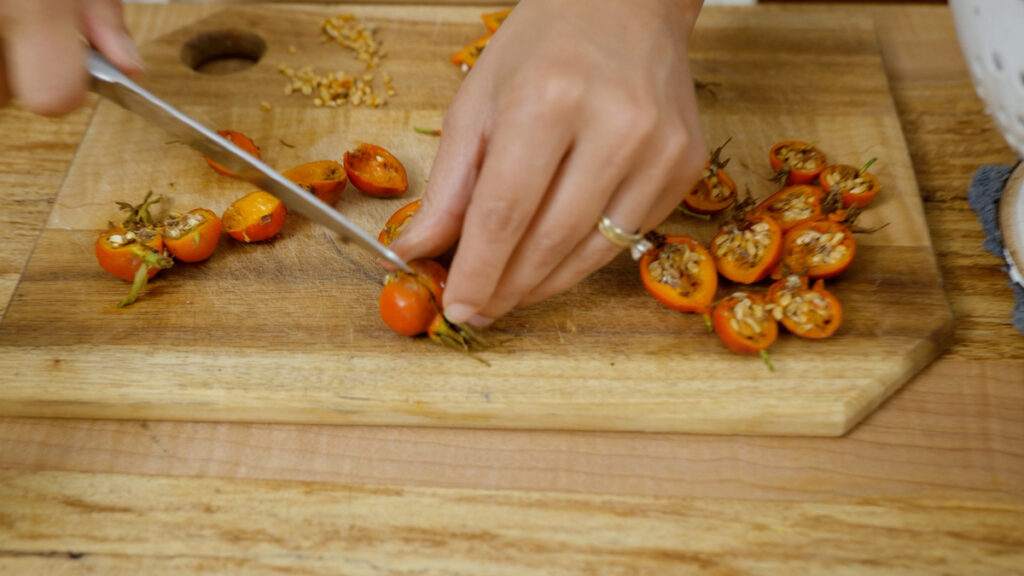 A woman's hand slicing a rosehip in half.