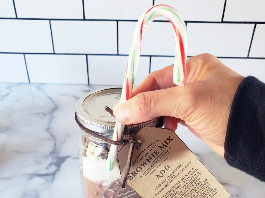 DIY Brownie mix in a mason jar with a hand attaching a candy cane to the jar.