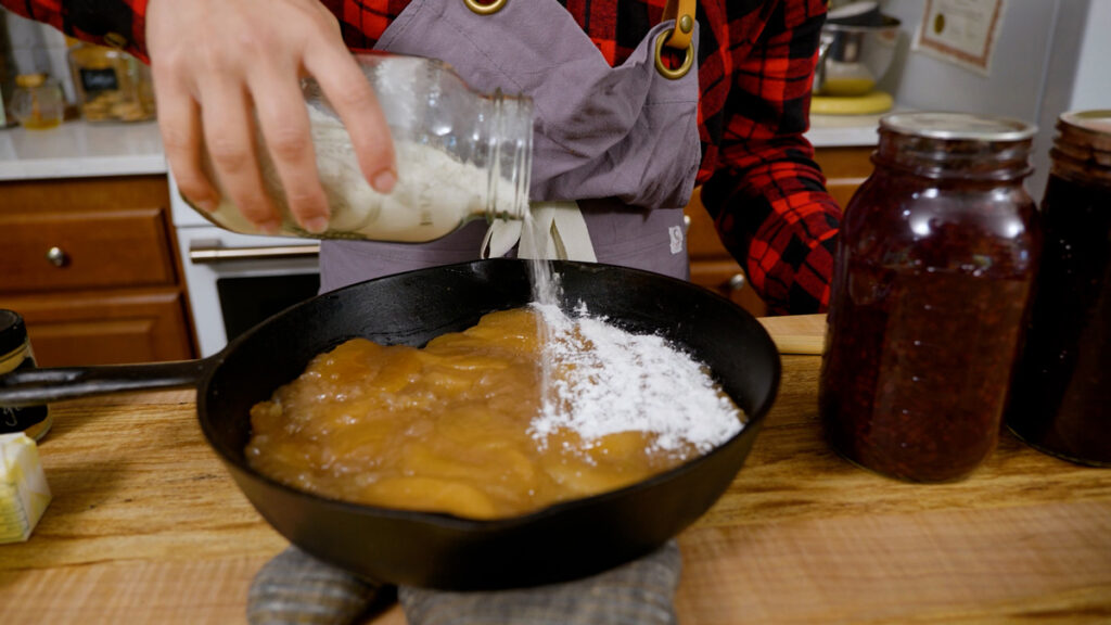 A woman pouring homemade cake mix over apple pie filling for a dump cake.