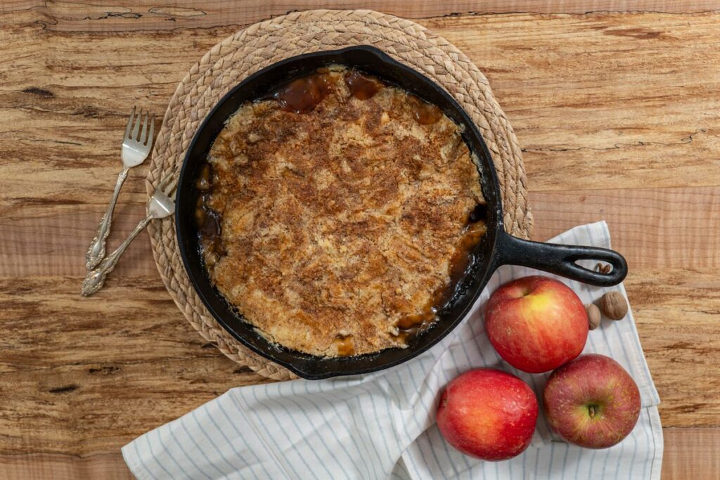 Apple dump cake in a cast iron pan with fresh apples.