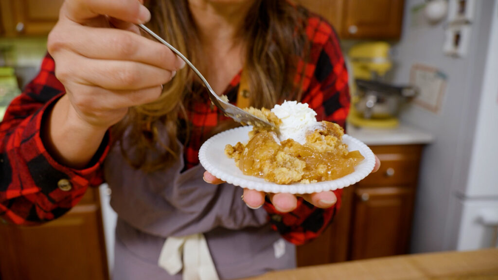 A woman taking a bite of an apple dump cake with whipped cream on top.