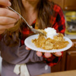 A woman taking a bite of an apple dump cake with whipped cream on top.