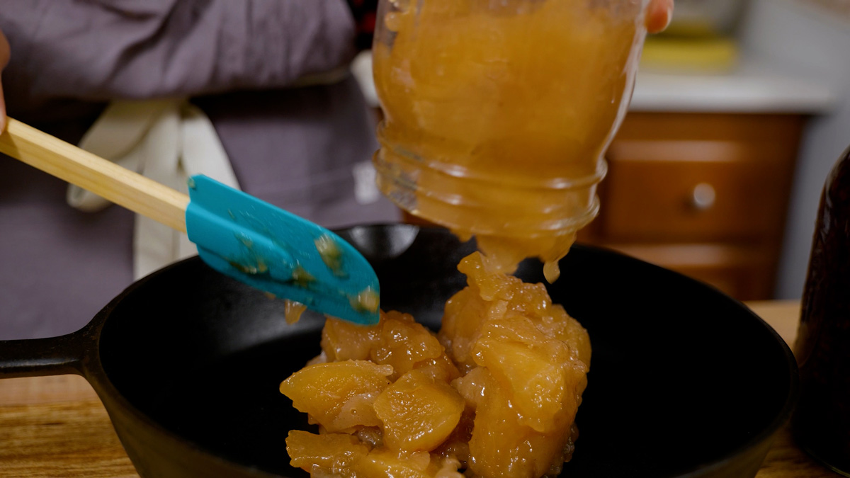Apple pie filling being poured into a cast iron pan.