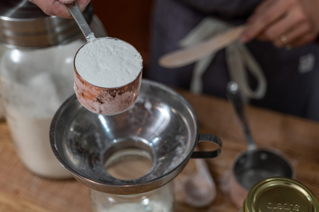 Ingredients being poured into a jar for homemade cake mix.