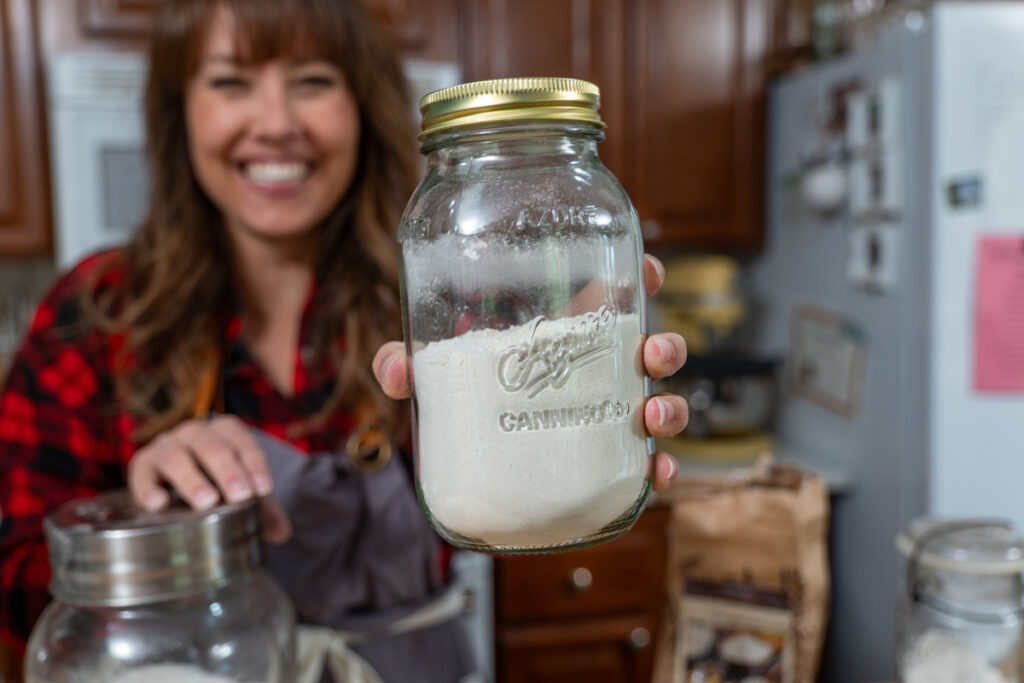 A woman holding up a Mason jar filled with homemade cake mix.