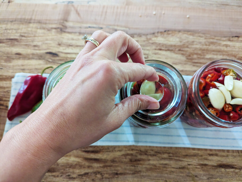 A woman adding a fermenting weight to a jar of peppers.