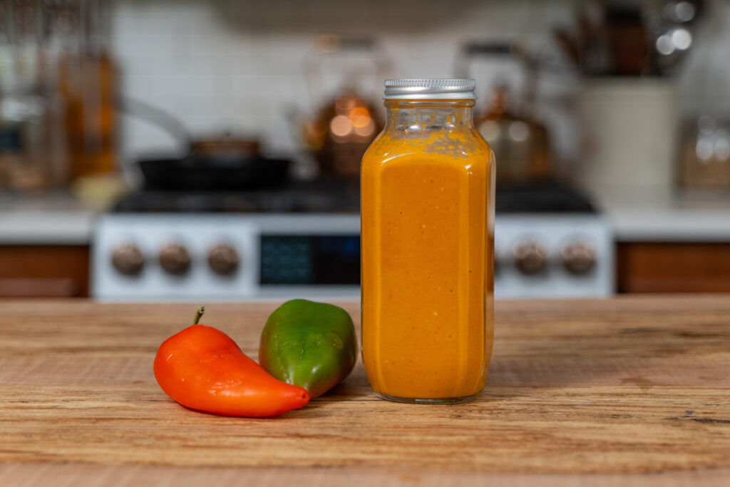 A jar of fermented hot sauce on a counter next to fresh peppers.