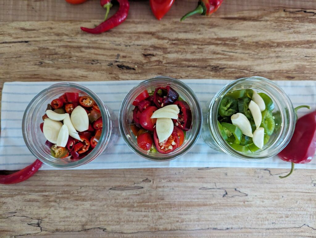 Vertical shot of three jars of hot sliced peppers on a wooden counter.