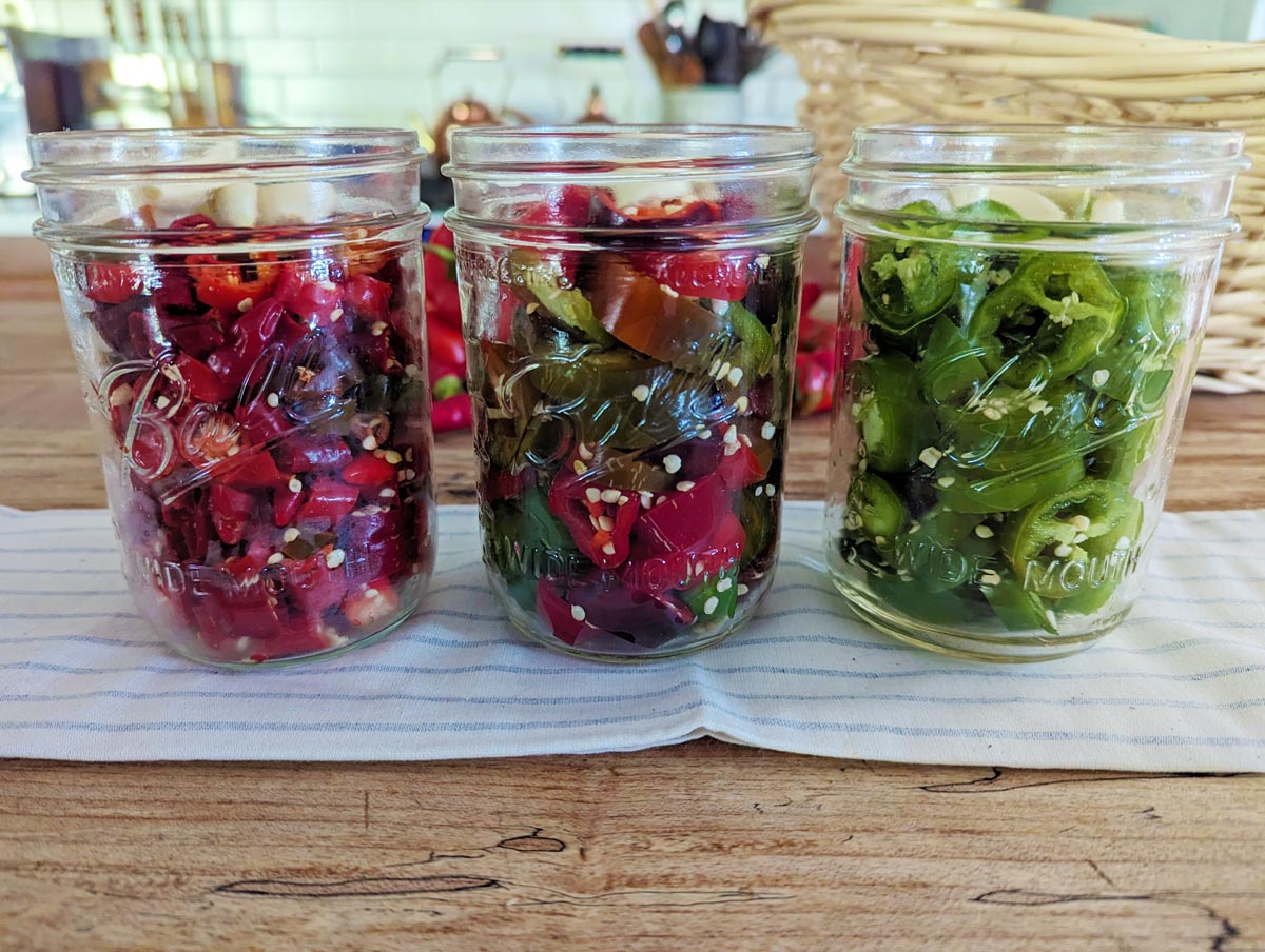 Three jars of hot sliced peppers on a wooden counter.