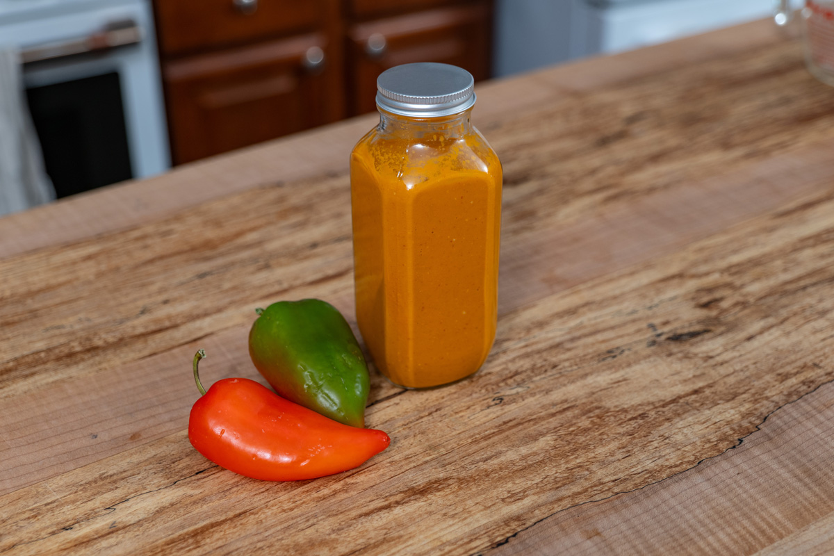 A jar of fermented hot sauce on a counter next to fresh peppers.