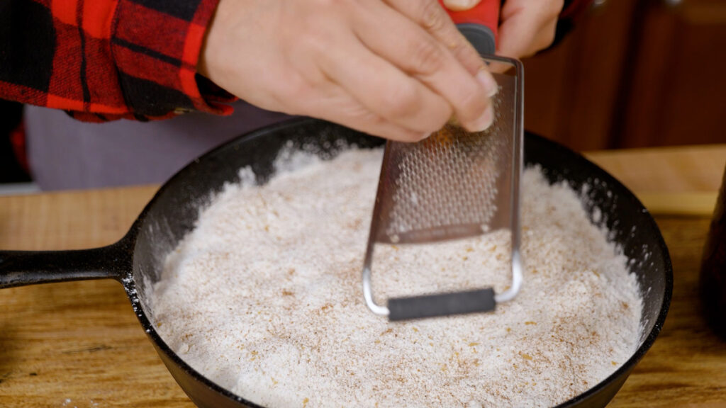 A woman grating nutmeg over the top of a dump cake.