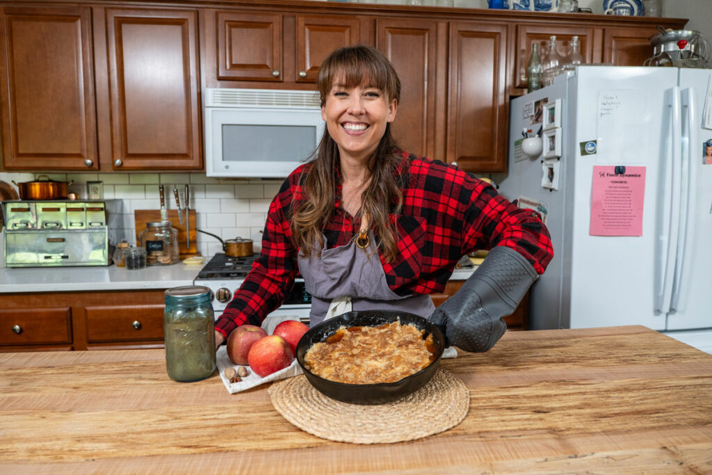 A woman holding up a cast iron skillet with apple dump cake.