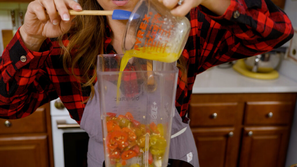 A woman adding melted butter to a blender.