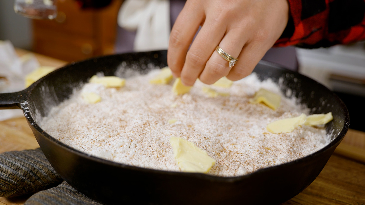A woman adding butter slices to the top of a dump cake.