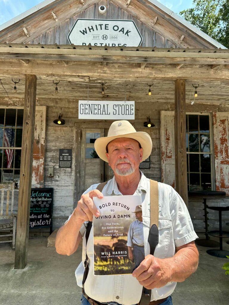 A man holding a book in front of White Oak Pastures general store.
