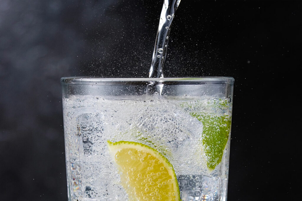 Soda water being poured into a glass with a lemon and lime slice.