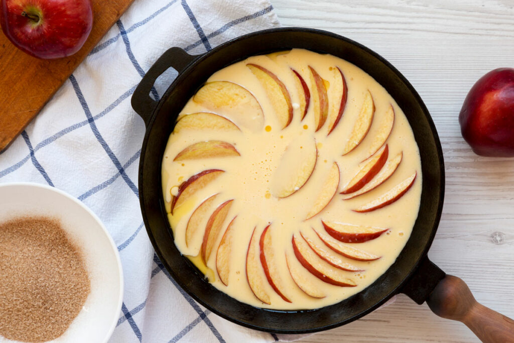 Sliced apples arranged in a pan of pancake batter.