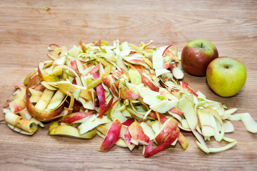 Two apples next to a pile of apple peels.