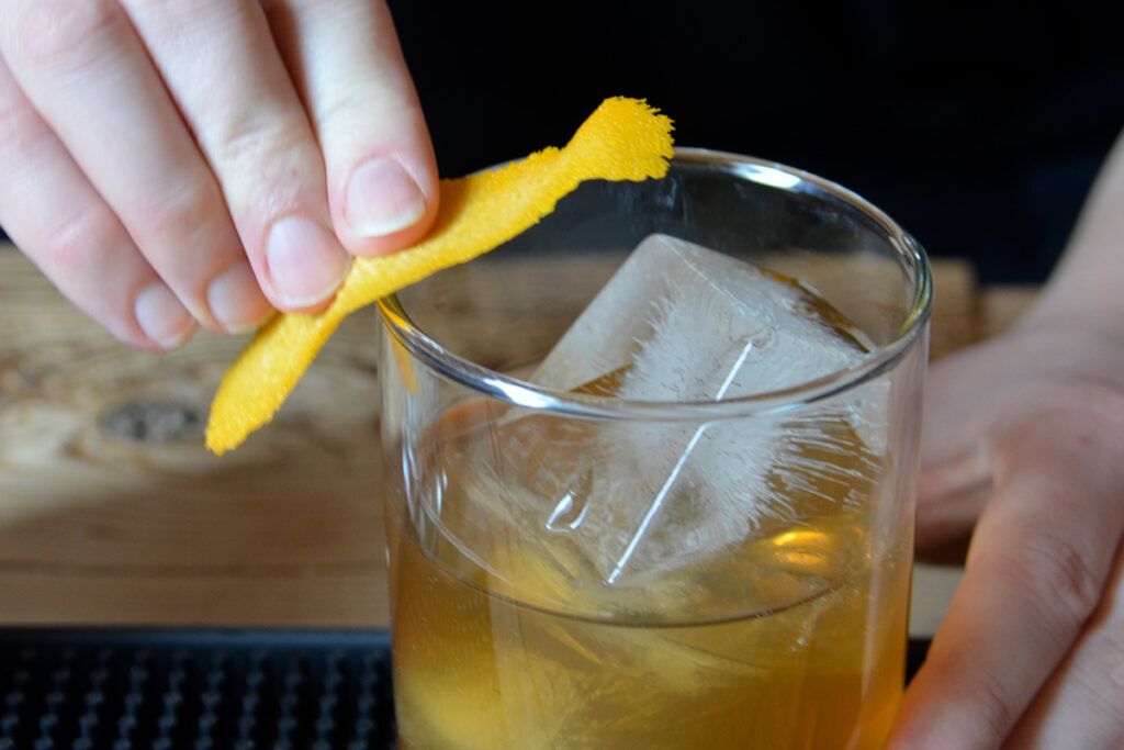 A lemon peel being wiped on a rim of a cocktail.