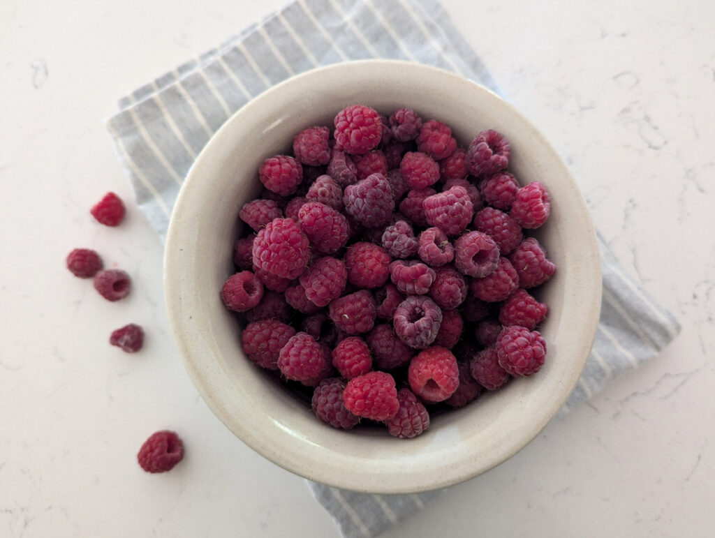 Freshly picked raspberries in a white bowl.