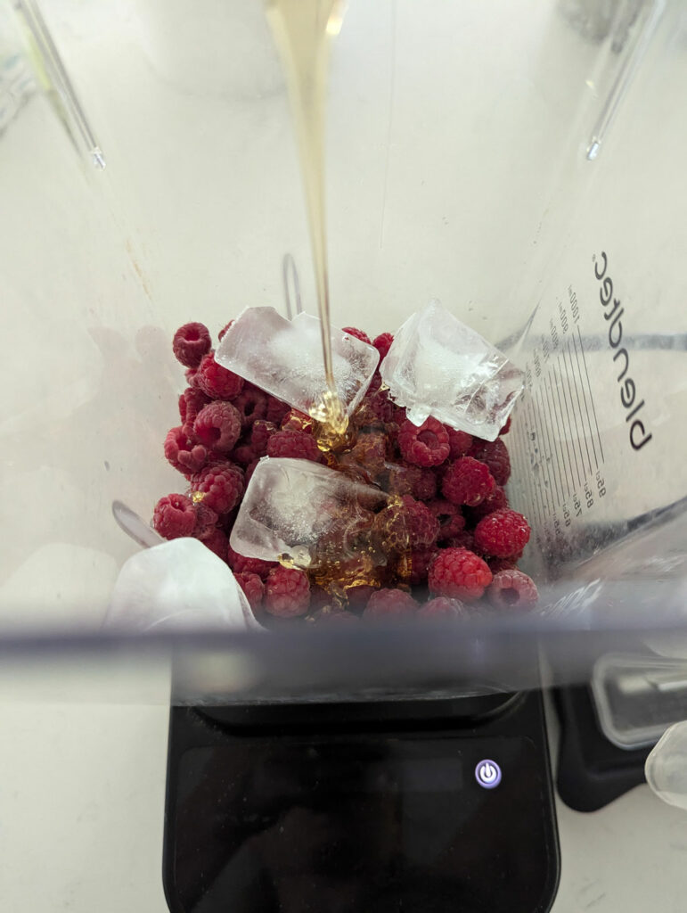 Raspberries and ice cubes with honey drizzling into a blender.