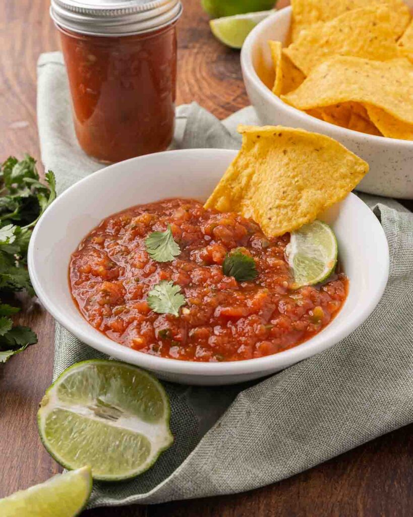 A white bowl full of fermented salsa garnished with cilantro, a wedge of lime and tortilla chip.