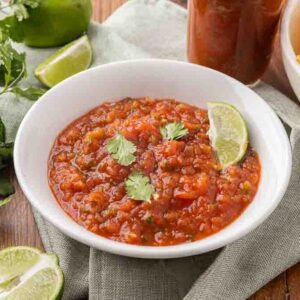 A white bowl full of fermented salsa garnished with cilantro and a wedge of lime.